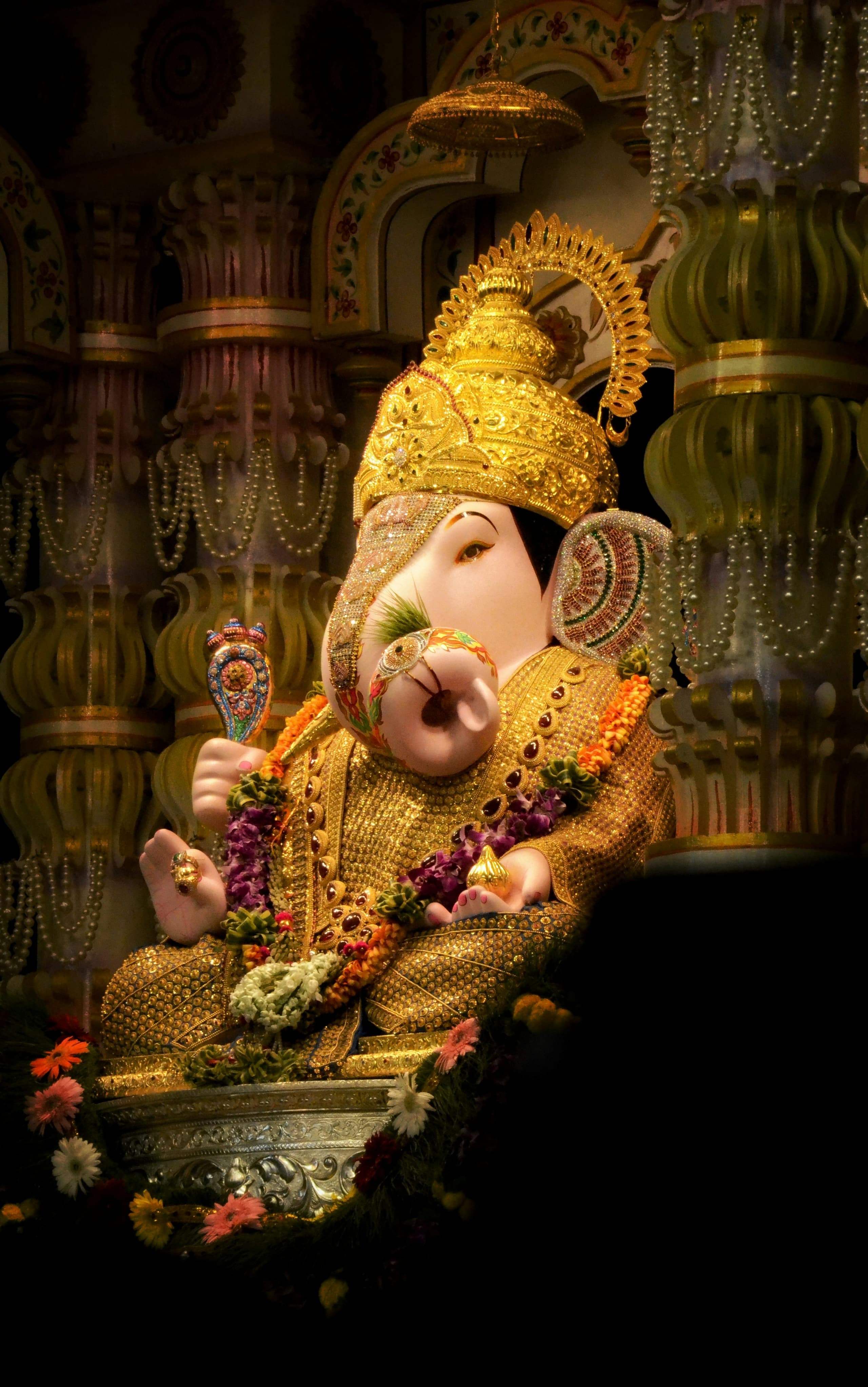 Lord Ganesha adorned in gold ornaments and fresh flower garlands inside a temple