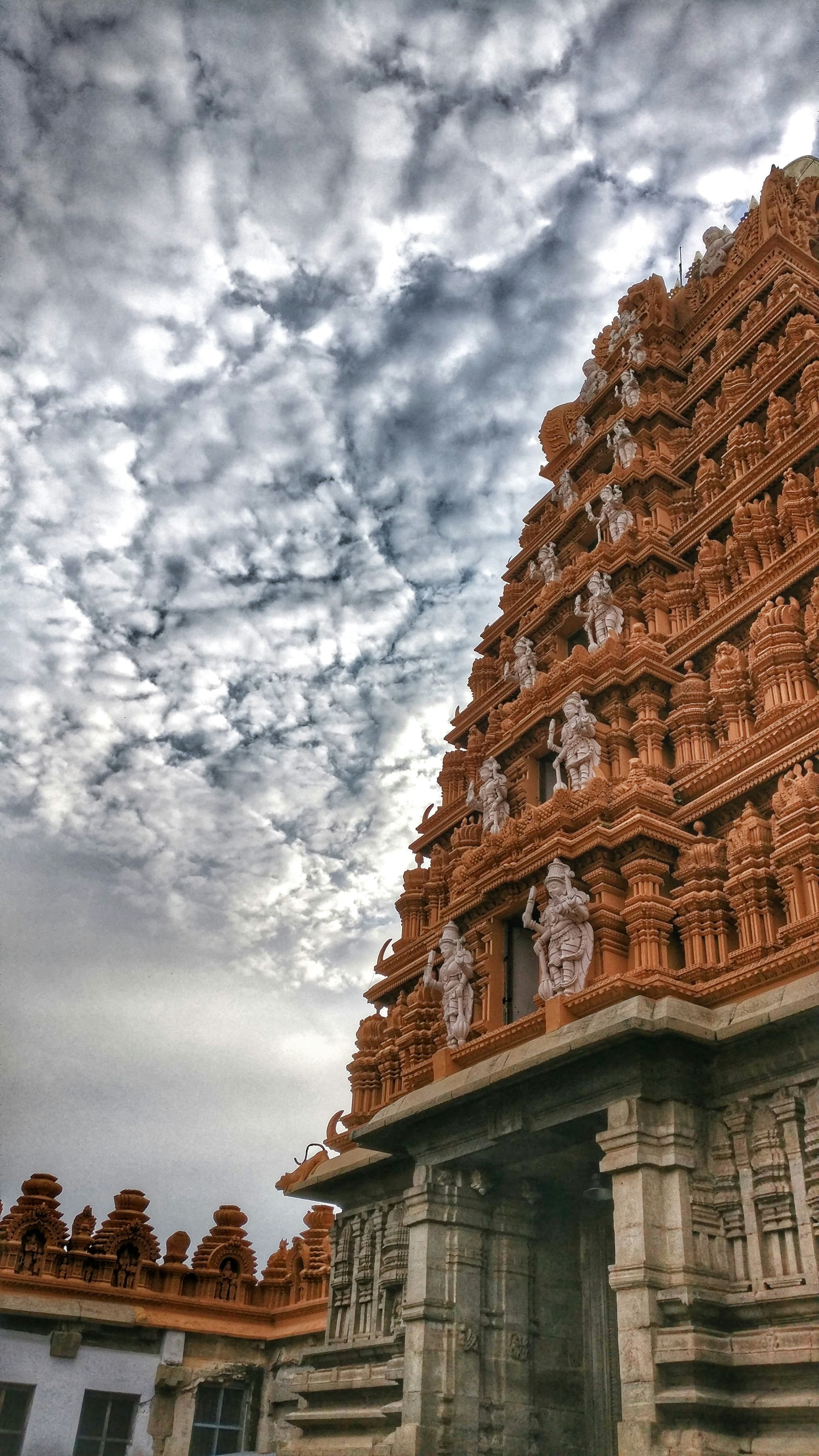 A terracotta temple gopuram rising against a dramatic cloud-filled sky