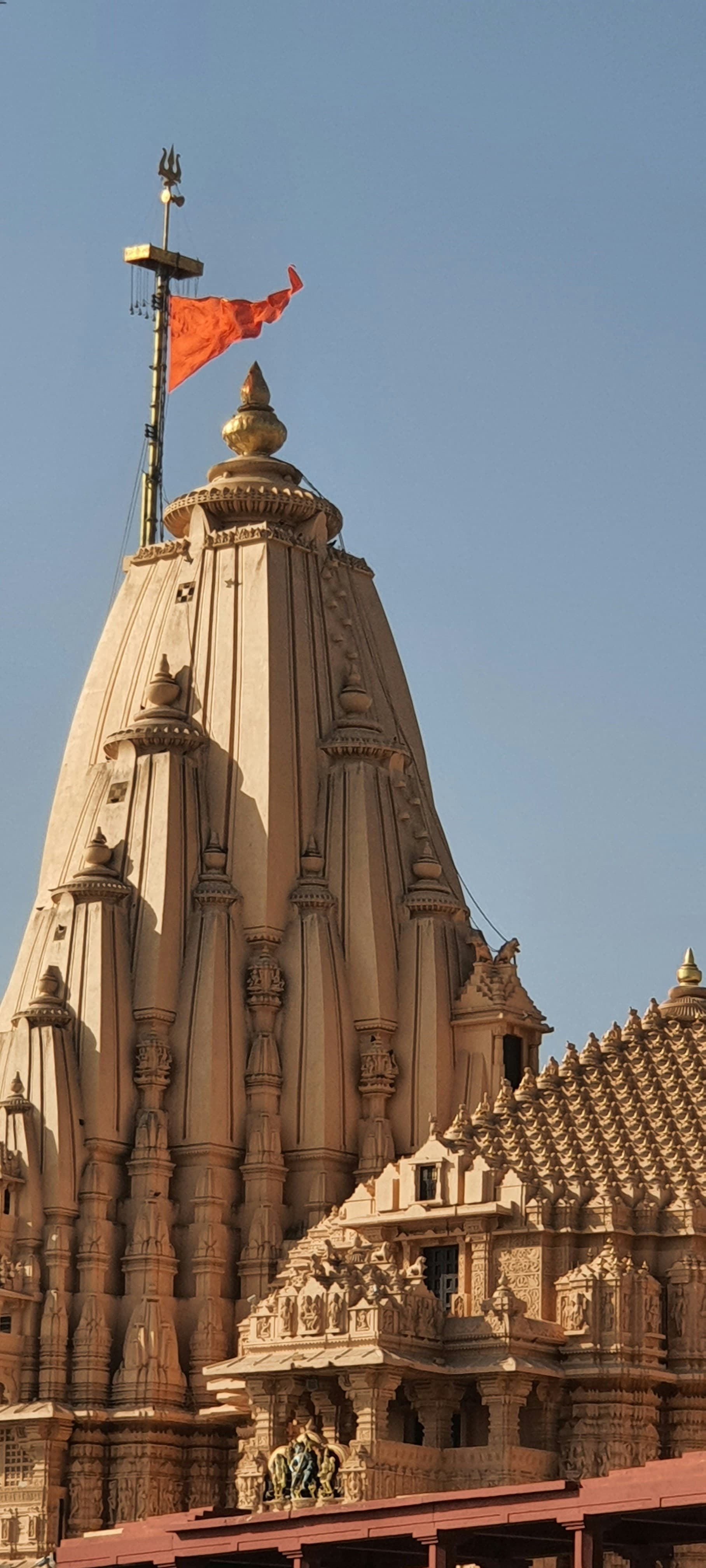 The carved shikhara of Somnath Temple with a saffron flag and trishul against a clear sky
